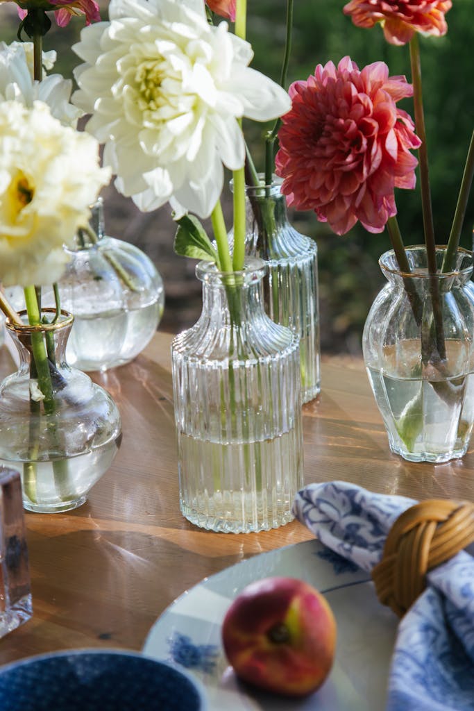 Elegant display of flowers in glass vases on a wooden table setting outdoors.