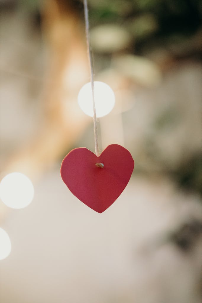 Close-up of a red paper heart hanging with warm bokeh light effects, creating a festive and romantic atmosphere.
