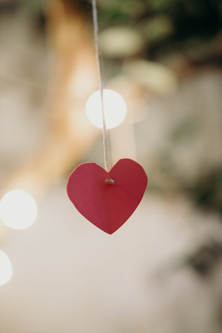 Close-up of a red paper heart hanging with warm bokeh light effects, creating a festive and romantic atmosphere.